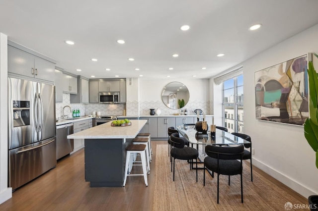 kitchen with stainless steel appliances, sink, gray cabinets, a kitchen island, and a breakfast bar area