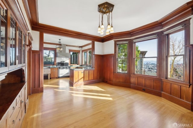 unfurnished dining area with light wood finished floors, a notable chandelier, wainscoting, and ornamental molding