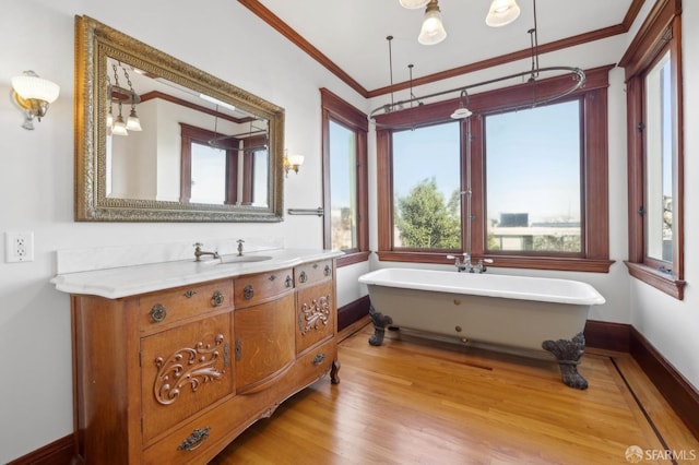full bath featuring baseboards, ornamental molding, wood finished floors, a soaking tub, and vanity