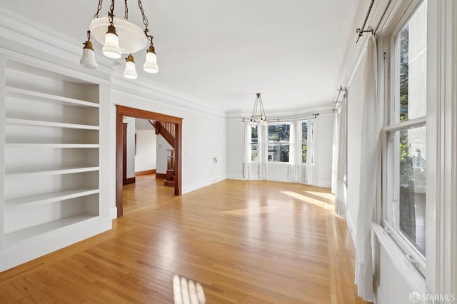 interior space with built in shelves, baseboards, light wood finished floors, ornamental molding, and a chandelier