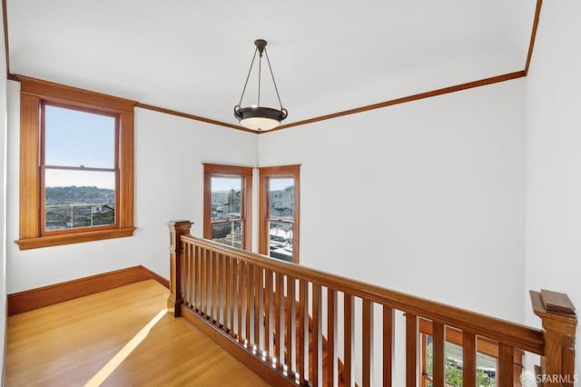 hall featuring a healthy amount of sunlight, crown molding, baseboards, an upstairs landing, and light wood-style flooring