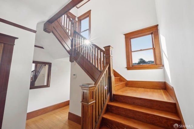 stairs with a high ceiling, wood finished floors, and baseboards