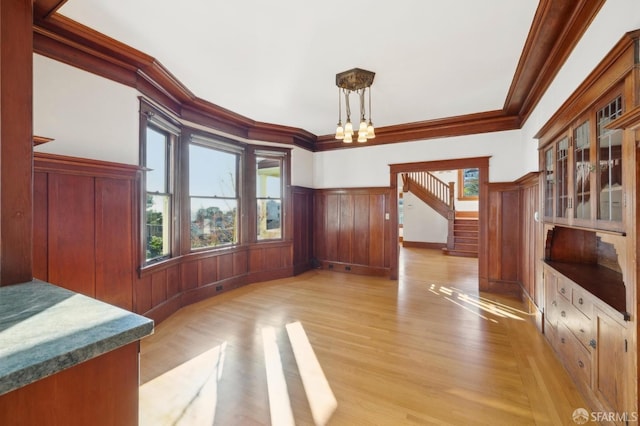 dining area featuring stairway, a wainscoted wall, light wood-type flooring, ornamental molding, and an inviting chandelier