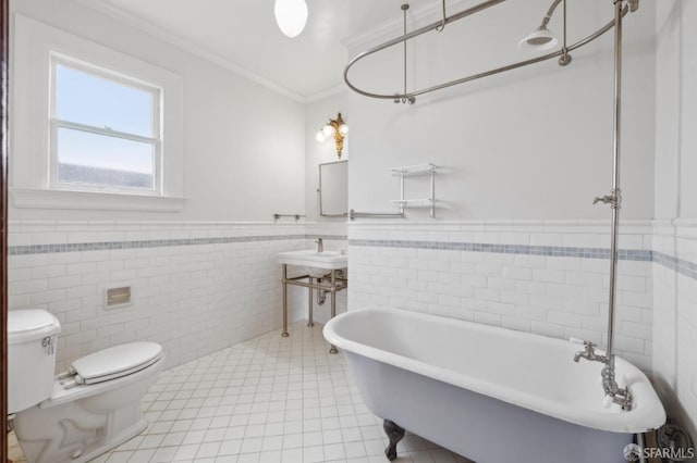 full bathroom with a freestanding tub, toilet, ornamental molding, wainscoting, and tile patterned flooring