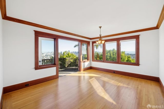 empty room featuring baseboards, a notable chandelier, wood finished floors, and crown molding