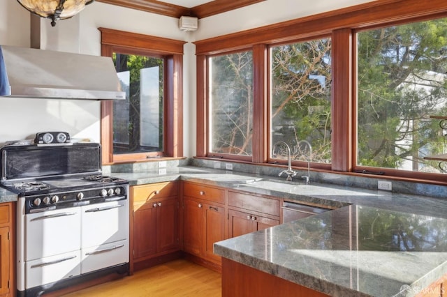 kitchen featuring range with two ovens, wall chimney exhaust hood, plenty of natural light, and a sink