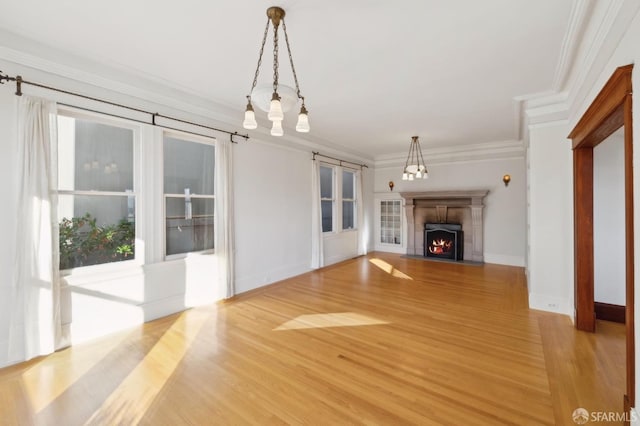 unfurnished living room with crown molding, light wood finished floors, baseboards, and a warm lit fireplace
