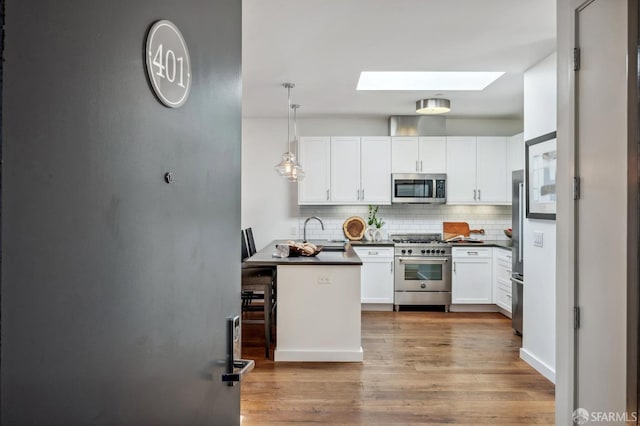 kitchen with tasteful backsplash, a skylight, appliances with stainless steel finishes, pendant lighting, and white cabinets