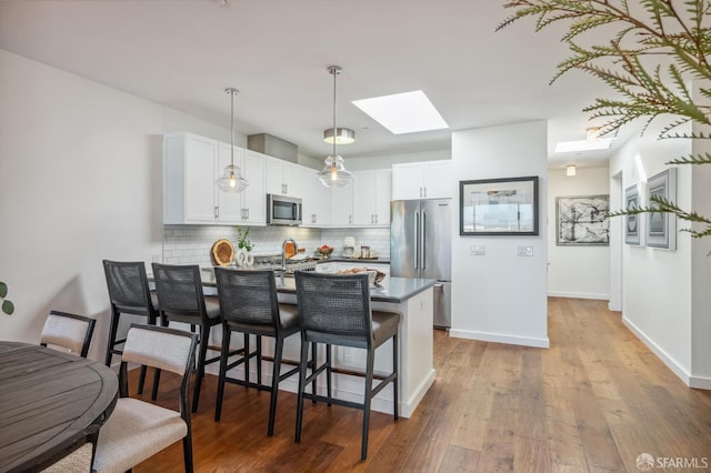 kitchen with a breakfast bar area, stainless steel appliances, white cabinets, decorative backsplash, and kitchen peninsula