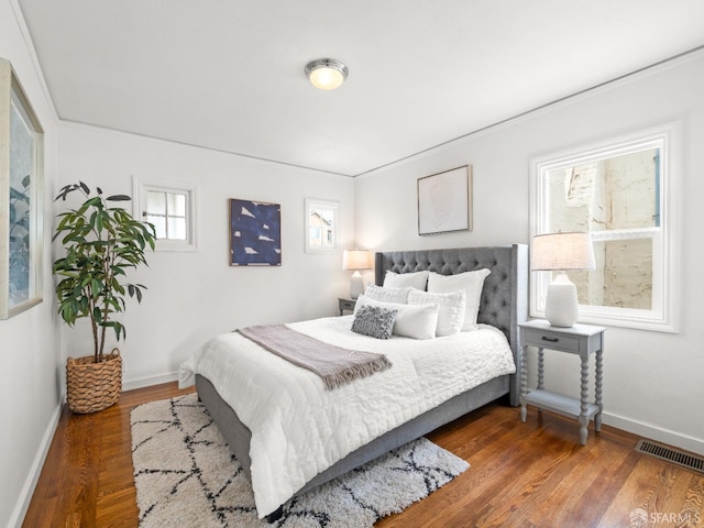 bedroom with baseboards, visible vents, and wood finished floors