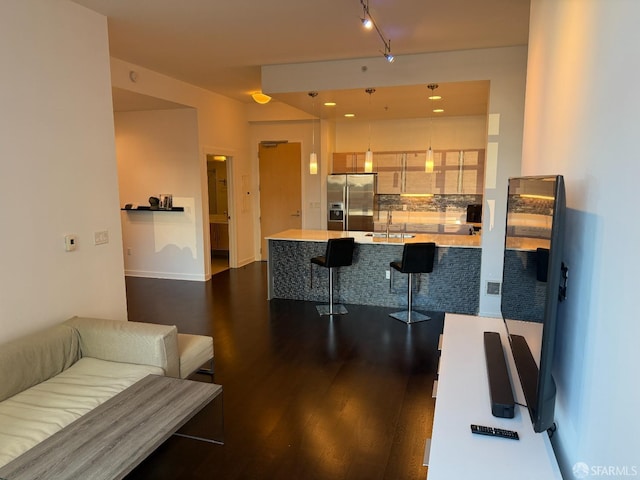 bar featuring stainless steel refrigerator with ice dispenser, dark wood-type flooring, decorative backsplash, and sink