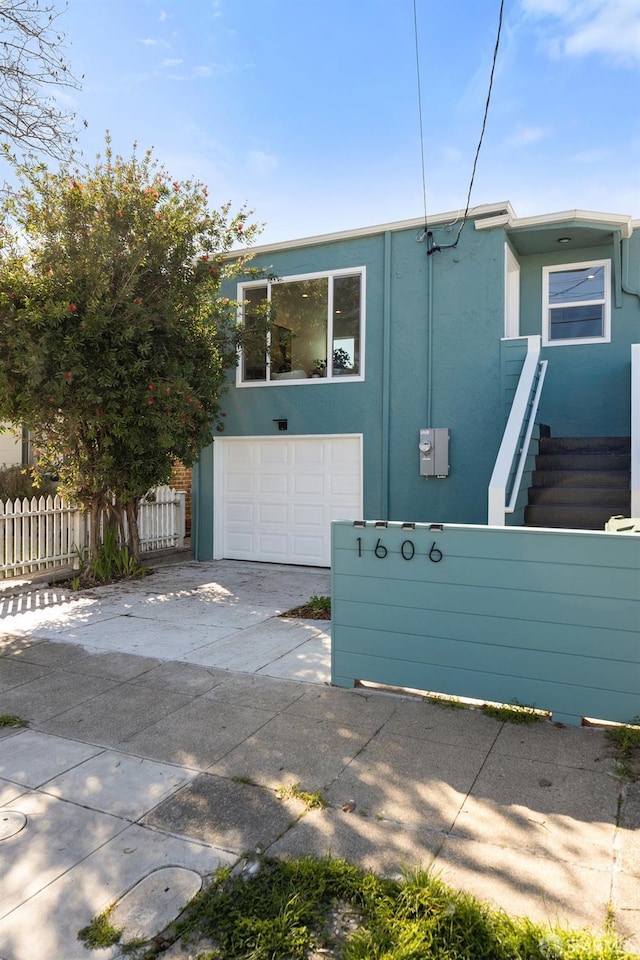 view of front of home with concrete driveway, fence, an attached garage, and stucco siding