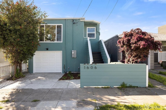 view of front of house featuring a garage, driveway, stairway, fence, and stucco siding