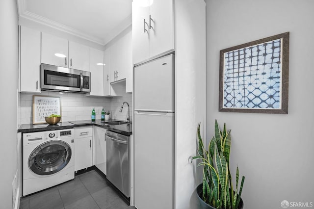 kitchen with appliances with stainless steel finishes, washer / dryer, sink, white cabinets, and backsplash