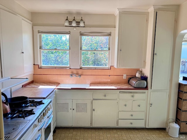 kitchen with sink, decorative backsplash, white gas range oven, and white cabinets