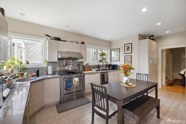 kitchen featuring stainless steel gas range oven, exhaust hood, beverage cooler, light hardwood / wood-style floors, and sink