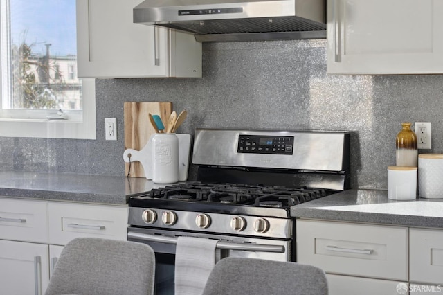 kitchen featuring stainless steel gas range, white cabinets, and wall chimney range hood