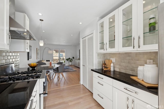 kitchen with light wood-style flooring, dark countertops, open floor plan, white cabinets, and wall chimney range hood