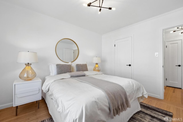 bedroom with baseboards, a notable chandelier, wood finished floors, and ornamental molding