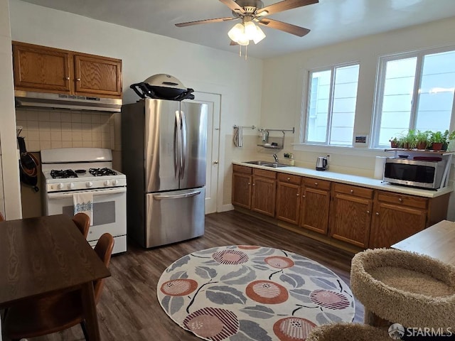 kitchen featuring stainless steel appliances, brown cabinets, dark wood-style floors, and under cabinet range hood