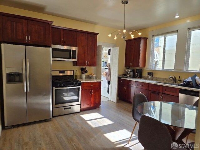 kitchen with dark brown cabinets, appliances with stainless steel finishes, an inviting chandelier, a sink, and light wood-type flooring