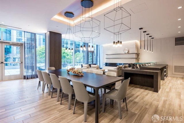 dining space with light wood-type flooring, expansive windows, and a raised ceiling