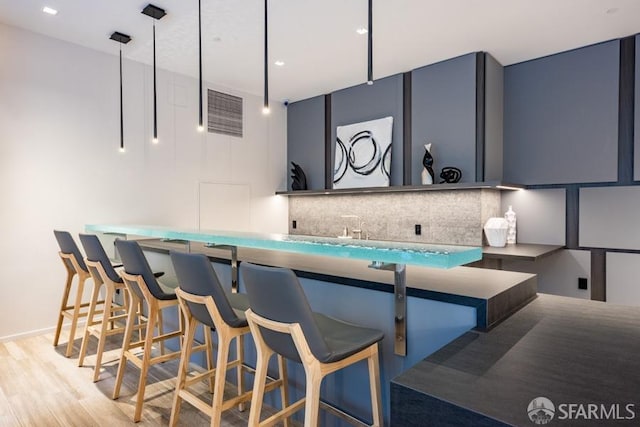 kitchen with tasteful backsplash, light wood-type flooring, blue cabinetry, decorative light fixtures, and a breakfast bar area