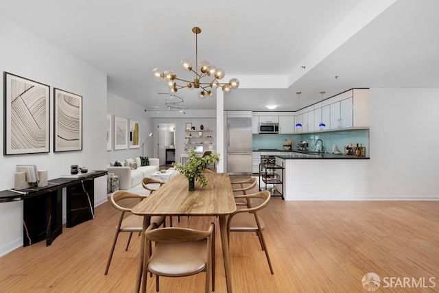 dining room with sink, light wood-type flooring, and an inviting chandelier