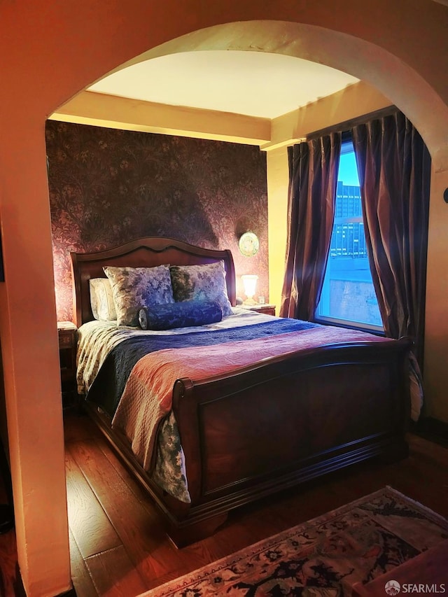 bedroom featuring arched walkways and wood finished floors