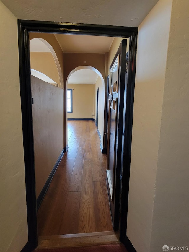 corridor with arched walkways, baseboards, and hardwood / wood-style flooring