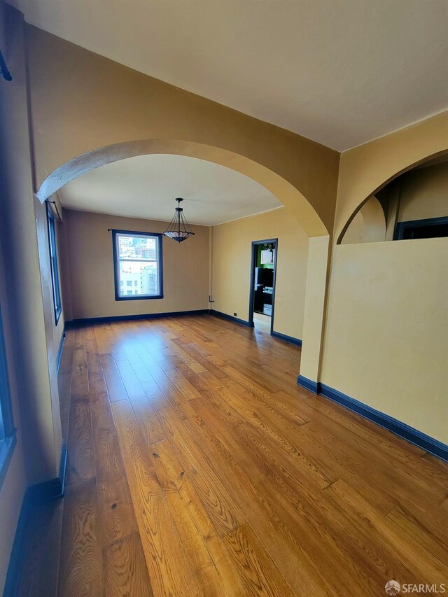 empty room with arched walkways, baseboards, and wood finished floors