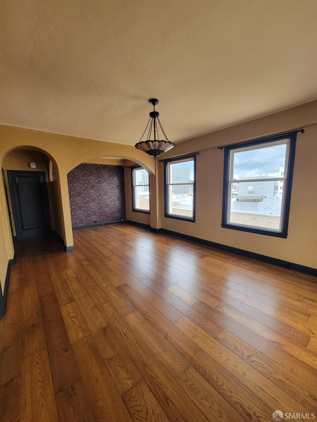 empty room featuring baseboards, arched walkways, and dark wood-style flooring