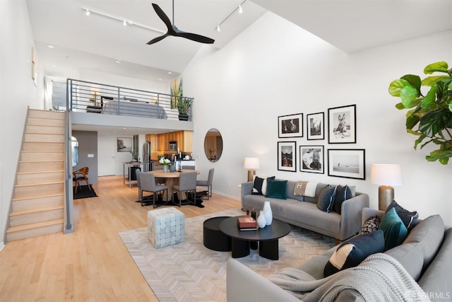 living room with light wood-type flooring, track lighting, ceiling fan, and a high ceiling