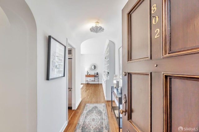 hall with light wood-type flooring, arched walkways, and baseboards