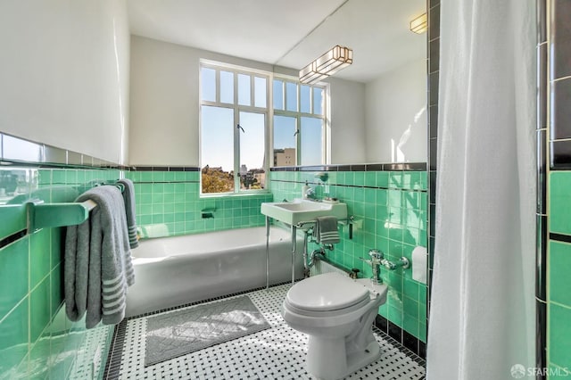 bathroom with a tub to relax in, tile patterned flooring, a wainscoted wall, a sink, and tile walls