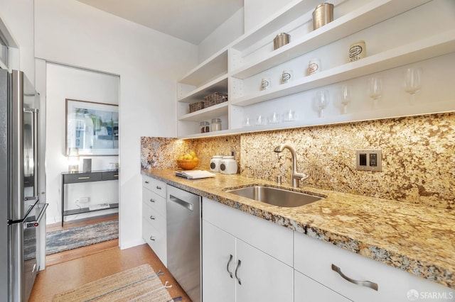 kitchen with light stone counters, open shelves, stainless steel appliances, decorative backsplash, and a sink