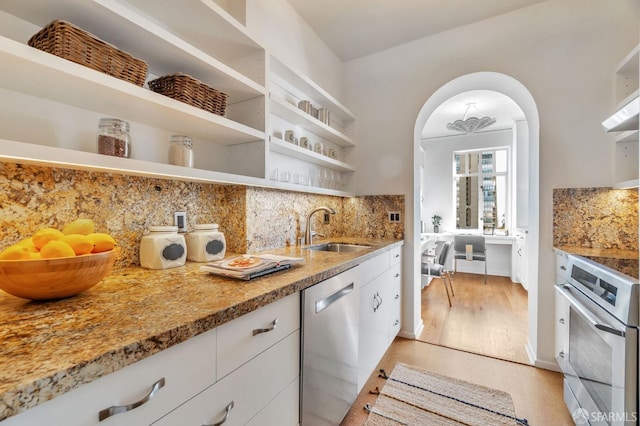 kitchen featuring tasteful backsplash, arched walkways, stainless steel appliances, open shelves, and a sink