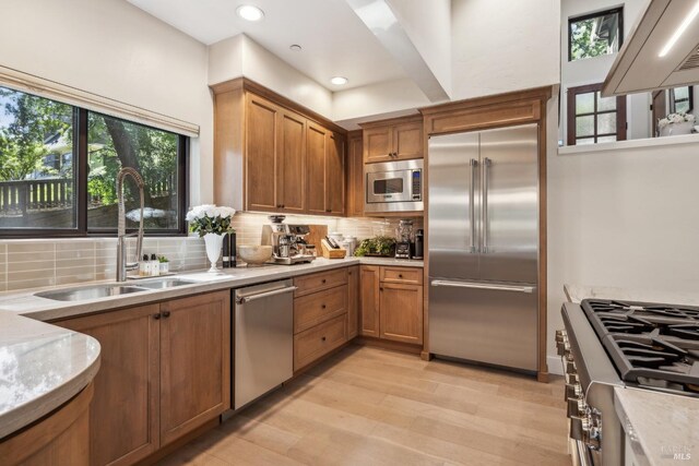 kitchen with light wood-style flooring, built in appliances, decorative backsplash, and a sink