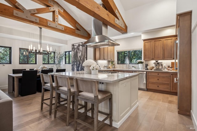 kitchen featuring stainless steel appliances, a chandelier, range hood, a breakfast bar, and high vaulted ceiling