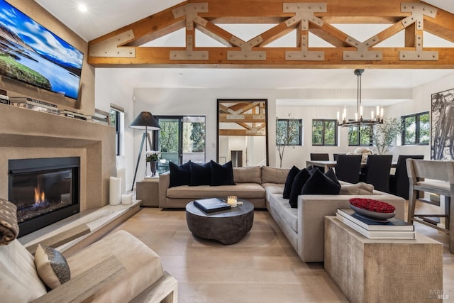 living area featuring a glass covered fireplace, high vaulted ceiling, a notable chandelier, and a healthy amount of sunlight