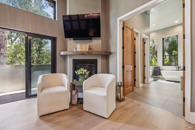 sitting room featuring a glass covered fireplace, plenty of natural light, and wood finished floors
