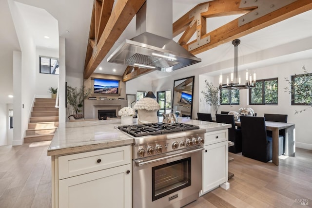 kitchen with light stone counters, island range hood, high end range, open floor plan, and a fireplace