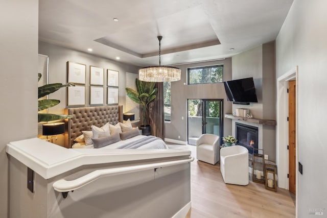bedroom featuring wood finished floors, a glass covered fireplace, an inviting chandelier, a raised ceiling, and recessed lighting