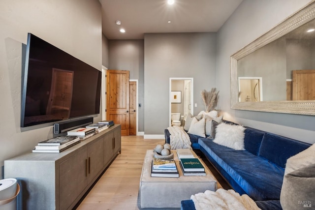living room with light wood finished floors, a high ceiling, baseboards, and recessed lighting