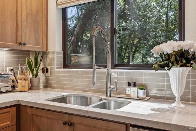 details featuring brown cabinetry, decorative backsplash, dishwasher, and a sink
