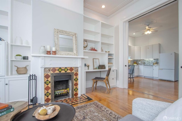 living room featuring light wood-style floors, ornamental molding, a ceiling fan, and a tile fireplace