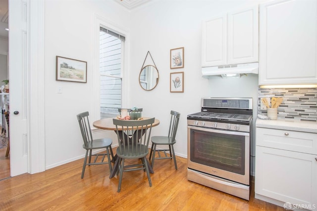 kitchen with under cabinet range hood, light countertops, stainless steel gas range oven, and white cabinetry