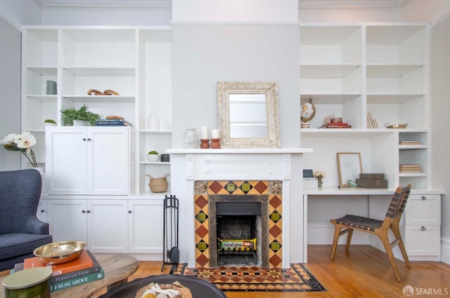 living area with light wood-style floors, built in shelves, and a tiled fireplace