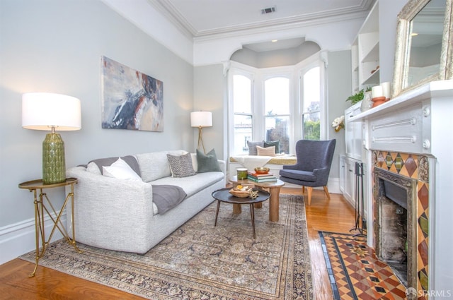 living room featuring crown molding, visible vents, a fireplace with flush hearth, wood finished floors, and baseboards