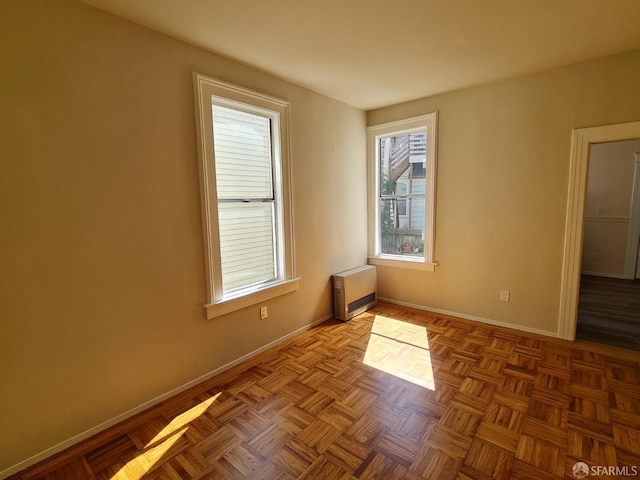 empty room with heating unit, a wealth of natural light, and light parquet floors